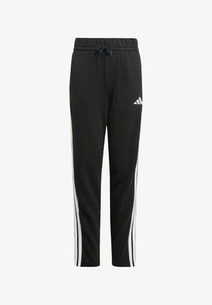Pantalones de chándal negros con cintura ajustable, con rayas laterales blancas y un logo de Adidas en el muslo izquierdo. El tejido parece suave y texturizado.