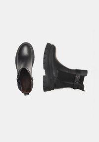 Bottines noires en cuir lisse avec un panneau texturé, semelle en caoutchouc épaisse et sangle réglable avec un accent métallique.
