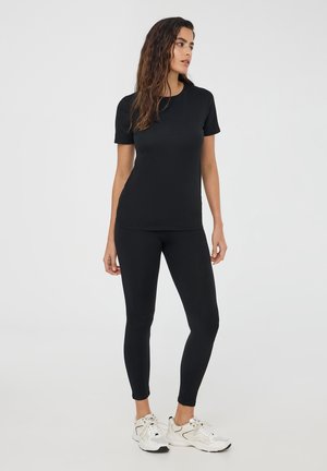 Maglietta sportiva nera e leggings, design aderente, texture liscia, abbinati a sneaker di colore chiaro; su uno sfondo neutro.