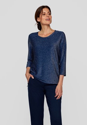 Navyblaue, glitzernde Bluse mit einem runden Ausschnitt und drei Viertelärmeln, lockere Passform, getragen mit dunklen Hosen, glatte Textur.