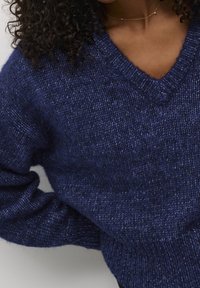 Navy blue knitted sweater with a v-neck and long sleeves. Texture appears soft, with a subtle heather pattern and ribbed cuffs.