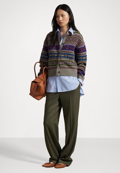 Gilet en tricot avec un motif Fair Isle multicolore, base grise, chemise col bleu, pantalon olive, sac en cuir marron et chaussures plates.
