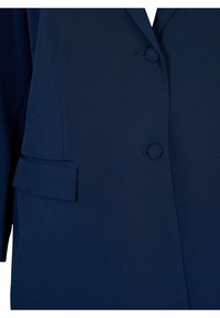 Mörkblå blazer med en strukturerad design, som har två runda knappar, en bröstficka och en sidoficka med klaff. Texturerad tygdetalj synlig.