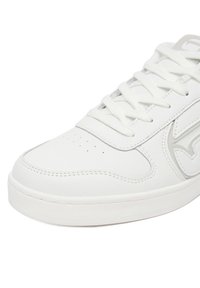 Zapatilla de cuero blanca con suela texturizada, parte delantera con cordones, caja de puntera perforada y detalle del logo en relieve en el panel lateral.