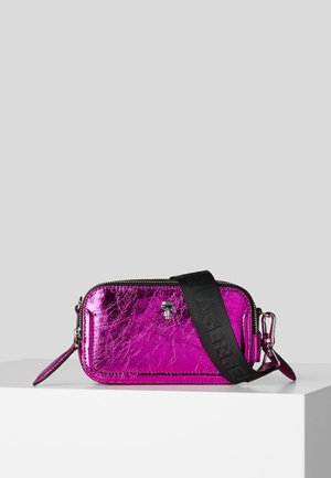 Mała metaliczna fioletowa prostokątna torebka na ramię z czarnym regulowanym paskiem i srebrnym zamkiem, ustawiona na białej powierzchni.