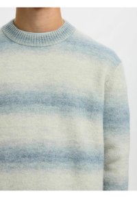 Pull avec des rayures horizontales bleu clair et blanches, col rond côtelé, porté par une personne cadrée du cou au milieu du torse.