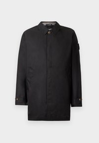 Cappotto impermeabile nero con colletto a punta, tasche laterali e polsini con bottoni. L'interno presenta un motivo a scacchi.