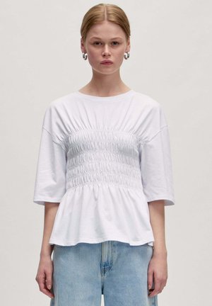Witte T-shirt met een geschroeid voorpaneel, korte mouwen en een peplumzoom. De stof lijkt zacht met een casual pasvorm. Wordt gekenmerkt door een combinatie met lichtblauwe denim.