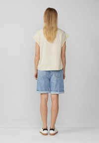 Lichtbeige kortemouwen top met een comfortabele pasvorm, gecombineerd met blauwe denimshorts met omgeslagen zomen en witte sneakers met zwarte accenten.