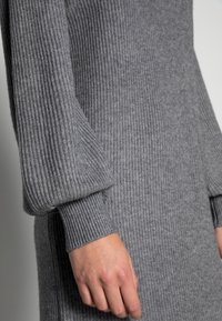 Abito grigio a coste con maniche lunghe e voluminose e polsini aderenti, che mette in risalto una consistenza morbida e una silhouette elegante.