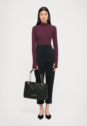 Black quilted tote bag with a chain strap and logo plaque, paired with a burgundy long-sleeve top and black tailored pants.