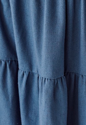 Miękka, teksturowana niebieska tkanina z marszczonymi detalami na szwach, tworząca warstwowy wygląd. Materiał wydaje się lekki i przewiewny.