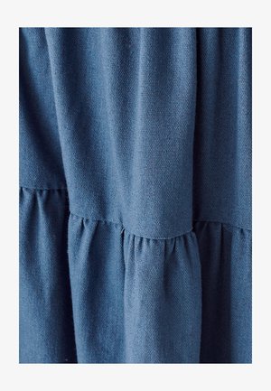 Pehme sinine kangas, millel on tekstuur ja kogumise detailid õmblustes, luues kihilise välimuse. Materjal näib olevat kerge ja hingav.