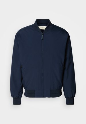 Veste bomber bleu marine en tissu lisse et léger, avec une fermeture éclair sur le devant, des poignets et un ourlet côtelés. Comprend des poches latérales zippées.