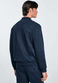 Felpa blu navy con scollo rotondo, polsini e orlo a costine e una texture liscia. Design minimalistico, senza motivi o accenti visibili.