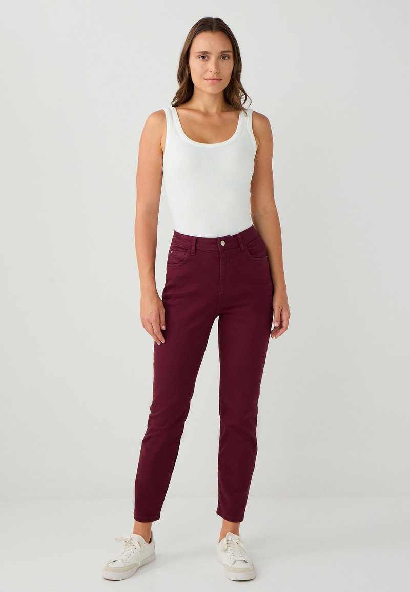 Jeans skinny bordeaux con una texture liscia, cinque tasche e chiusura a bottone. Abbinati a un top a canotta bianco a coste e sneakers bianche.