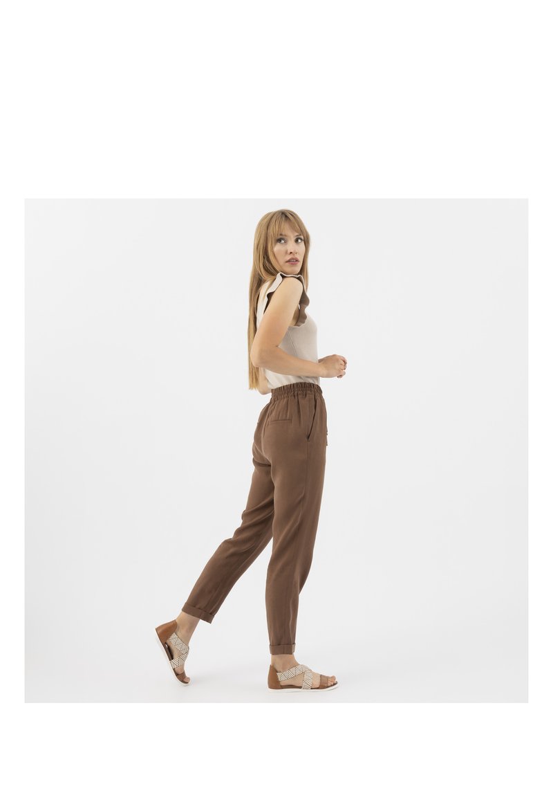 Hnědé, lehké kalhoty s elastickým pasem, zúženými nohavicemi, bočními kapsami a měkkou texturou. Kombinované s sandály s tkaným designem.