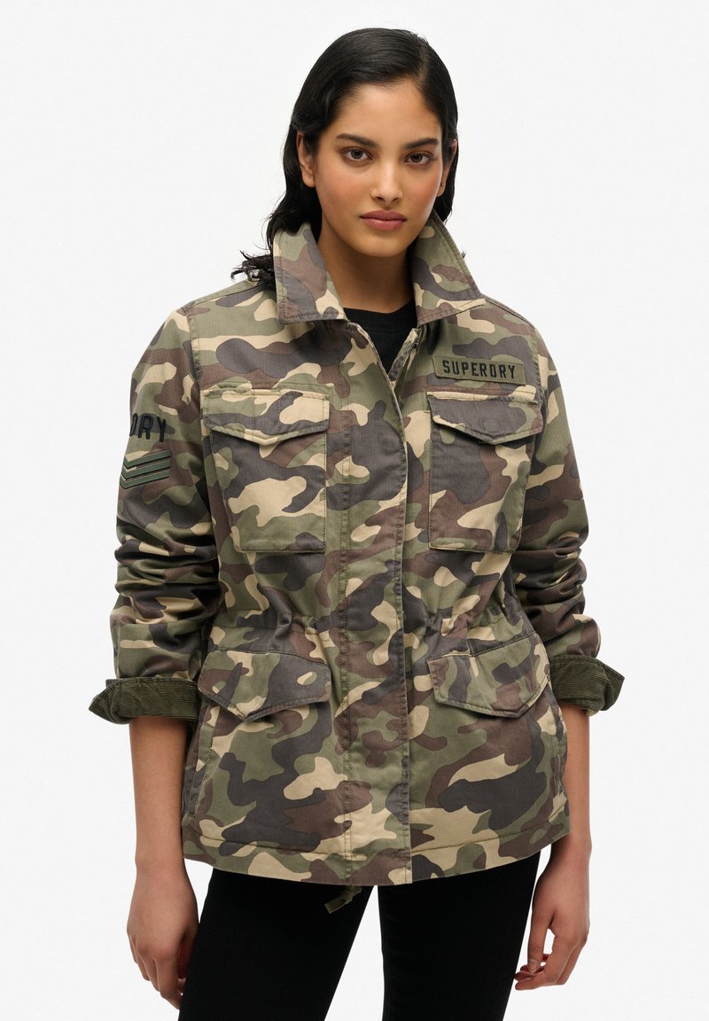 Veste camouflage en vert, marron et beige avec un bouton sur le devant, quatre poches et un col. Présente le logo 'SUPERDRY' sur la poitrine et la manche.