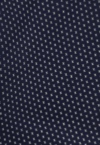 Nawodna tkanina z małym, powtarzającym się białym wzorem geometrycznym. Tekstura jest gładka z lekkim rozciąganiem, co zapewnia miękkie wrażenie.