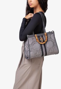 Borsa a tracolla grigia trapuntata con motivo floreale, con manico in bambù color oro e dettagli verticali neri, abbinata a una tracolla grigia.