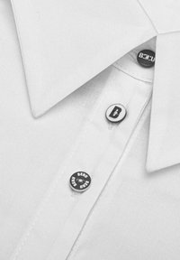 White collared shirt with a textured fabric. Features black buttons with "B" and "BEND" text. Clean design, emphasizing simplicity and detail.