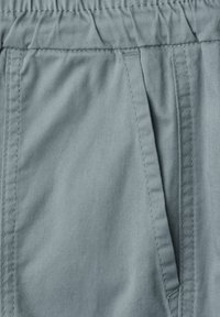 Gros plan sur un pantalon en tissu gris clair avec une taille élastique et une poche latérale avec des détails de couture visibles.