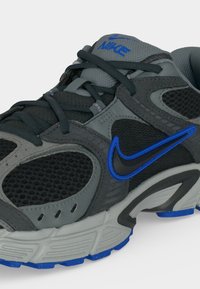 Γκρι και μαύρο παπούτσι για τρέξιμο Nike με μπλε accent, δίχτυα και κορδόνια, επισημαίνοντας το πλαϊνό λογότυπο και την μαλακή σόλα.