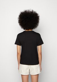 Camiseta de algodón negra de manga corta y cuello redondo, con una textura suave y un diseño básico, combinada con pantalones cortos de color claro.