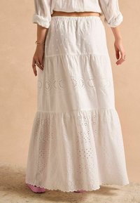 Witte katoenen maxi-rok met geborduurde patronen, gelaagde ruches en een geschulpte zoom. Elastische tailleband voor comfort.