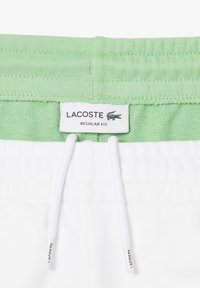 Pantaloni corti bianchi con una vita elastica verde chiaro, dotati di un cordino e un'etichetta con il logo Lacoste, in un design a vestibilità regolare.