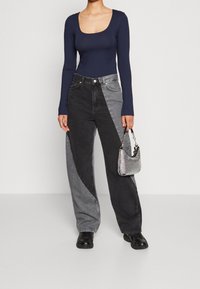 Marinblå långärmad topp med rundad halsringning, kombinerad med vida jeans som har en diagonalt svart och grå färgblockering. Liten silverhandväska.