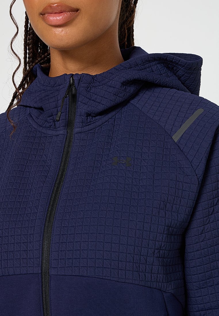 Chaqueta con capucha de color azul marino con textura acolchada, que cuenta con una cremallera completa y un sutil logo negro en el pecho. Acentuada con detalles en gris.