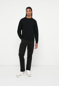Maglione nero a trama, pantaloni cargo neri a vestibilità ampia e sneakers bianche con dettagli grigi. Design minimalista, senza motivi o dettagli evidenti.