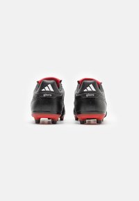 Des chaussures de football noires avec une texture lisse, arborant des accents rouges sur le talon et la semelle, et trois bandes blanches à l'arrière.