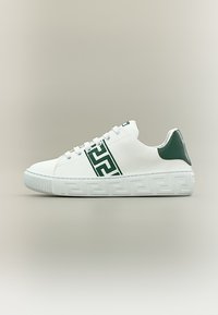 Baskets basses blanches avec une bande géométrique verte sur le côté et un passant vert assorti à l'arrière, semelle embossée à motif, et lacets blancs.