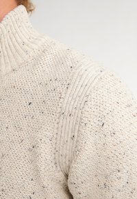 Maglione lavorato a maglia color crema con colletto a coste, caratterizzato da una texture screziata e da motivi sottili su tutto il tessuto.