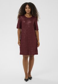 Burgundijska haljina s šljokicama, kratkim rukavima, okruglim izrezom i ravnim krojem. Glatka tekstura s blistavim akcentima. Crne cipele na špic.