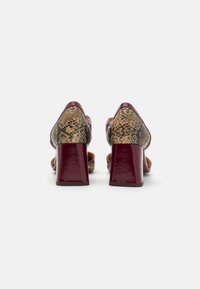 Chaussures à talons bordeaux avec une finition brillante, présentant un dos en textile à motif de peau de serpent. Talon large pour une bonne stabilité. Conception à bout ouvert.
