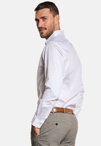 Weißes Langarmhemd mit klassischem Kragen, kombiniert mit grauen, strukturierten Hosen und einem braunen Gürtel, mit einem Knopfdetail an der Hose.