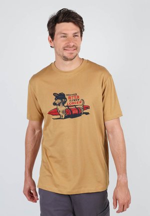 T-shirt beige à manches courtes avec un graphique d'un chien et d'une planche de surf, avec le texte : "PLUS DOUX, MEILLEUR, PLUS LENT, PLUS LONG." Matériau en coton doux.