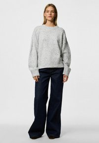 Grått marmorerat stickat tröja med sänka axlar, ribbat avslut och breda ärmslut, kombinerat med mörka vida jeans. Enkel, minimalistisk design.