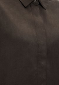 Σκούρο καφέ πουκάμισο με γιακά, κρυφή πατιλέτα με κουμπιά και ένα ορατό επάνω κουμπί.