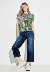 Top corto a maniche corte a righe verdi e nere abbinato a jeans a gamba larga di un blu scuro e sneaker chiare. Design semplice e vestibilità rilassata.