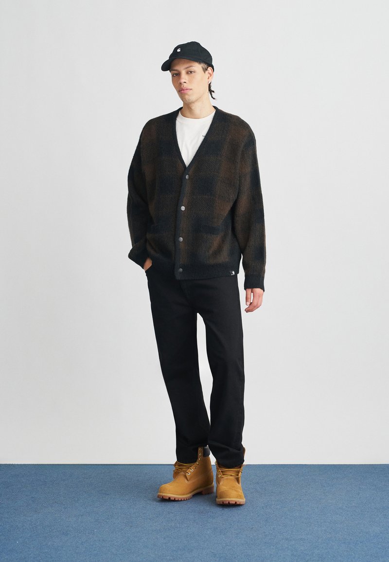 Black and brown patterned cardigan with a V-neck, button closure, and pockets, paired with black pants and tan lace-up boots.