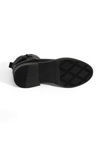 Bottines noires avec une semelle en caoutchouc texturé, un talon courbé et une fermeture éclair sur le côté. Tige en cuir lisse avec des détails de couture subtils.