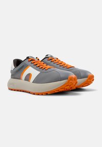 Scarpe da ginnastica grigie con lacci e dettagli arancioni, dotate di una tomaia testurizzata e di una suola ammortizzata con punti di presa sporgenti.
