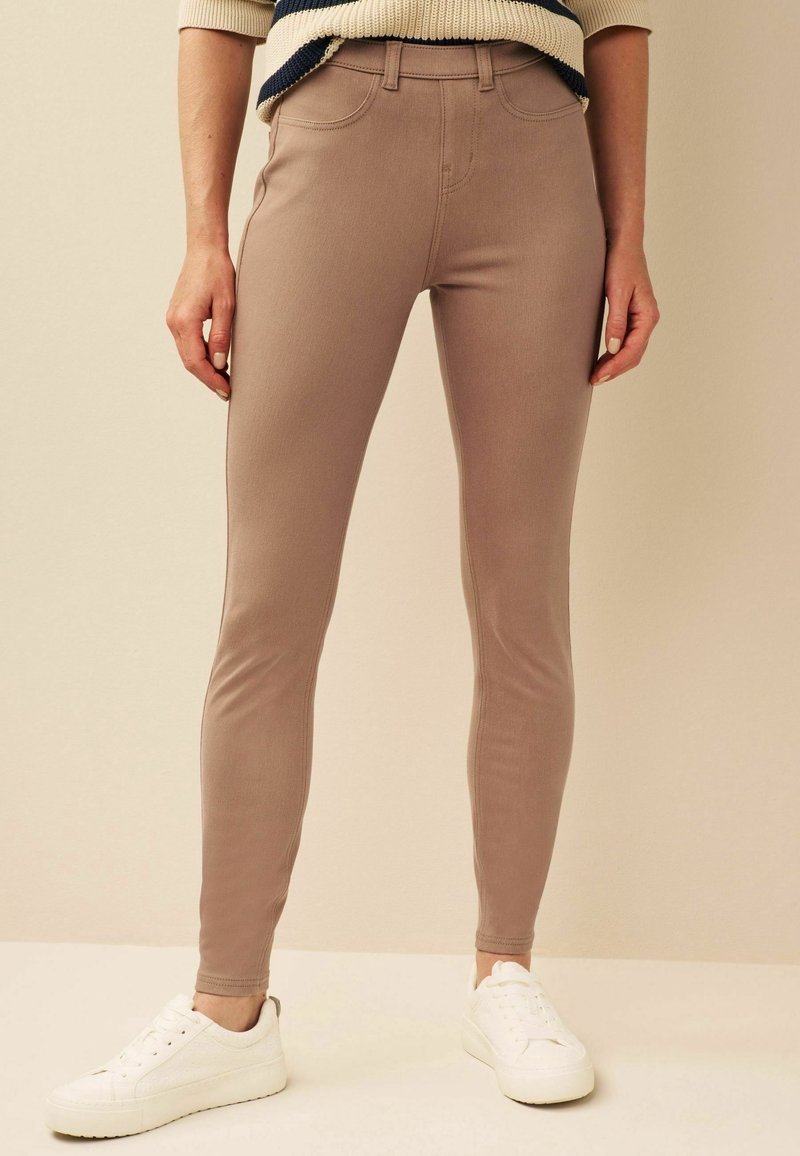 Pantalon beige ajusté porté avec des baskets blanches et un pull court rayé beige et noir sur un fond neutre.