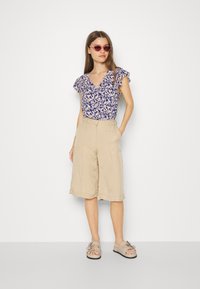 Top com padrão floral e mangas com folhos, combinado com culotes bege e sandálias claras. O conjunto apresenta um corte descontraído e texturas suaves.