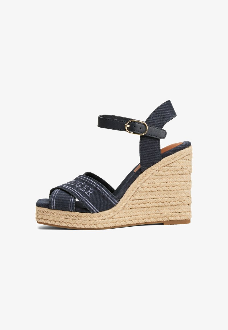 Navy fabric wedge sandals with a braided jute heel and ankle strap. Features a crossed strap design and embossed branding on the upper.