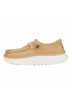 Botte slip-on en toile beige avec une surface texturée, semelle en caoutchouc blanc et système de laçage élastique. Présente un logo discret à l'arrière.